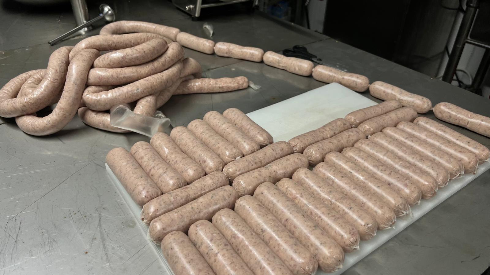 Freshly made farm sausages laid out on a stainless steel table